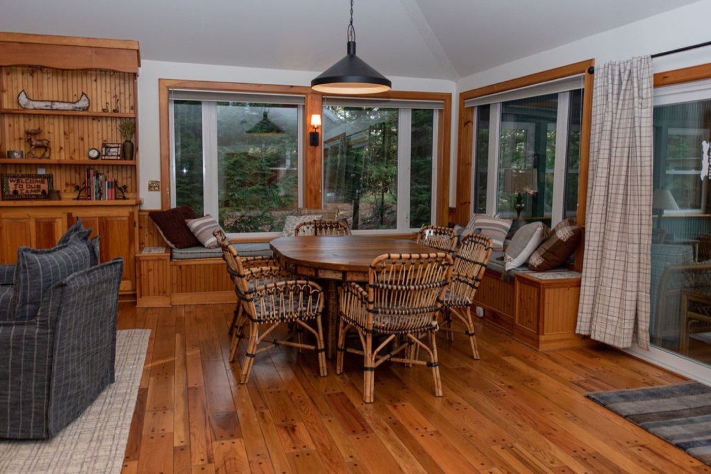 A dining nook at Camp Sunnyside with a wooden table, rattan chairs, window seat, and a canoe paddle displayed on the built-in shelf.