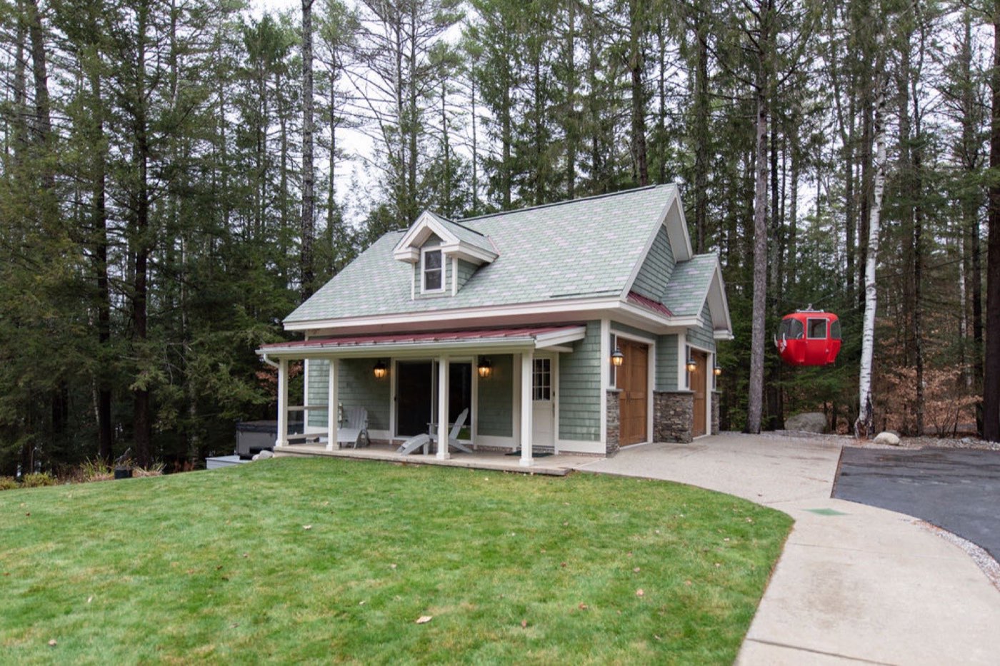 The sage-shingled Game House at Camp Sunnyside among the pines, with a covered porch, hot tub, and the red gondola beside it.