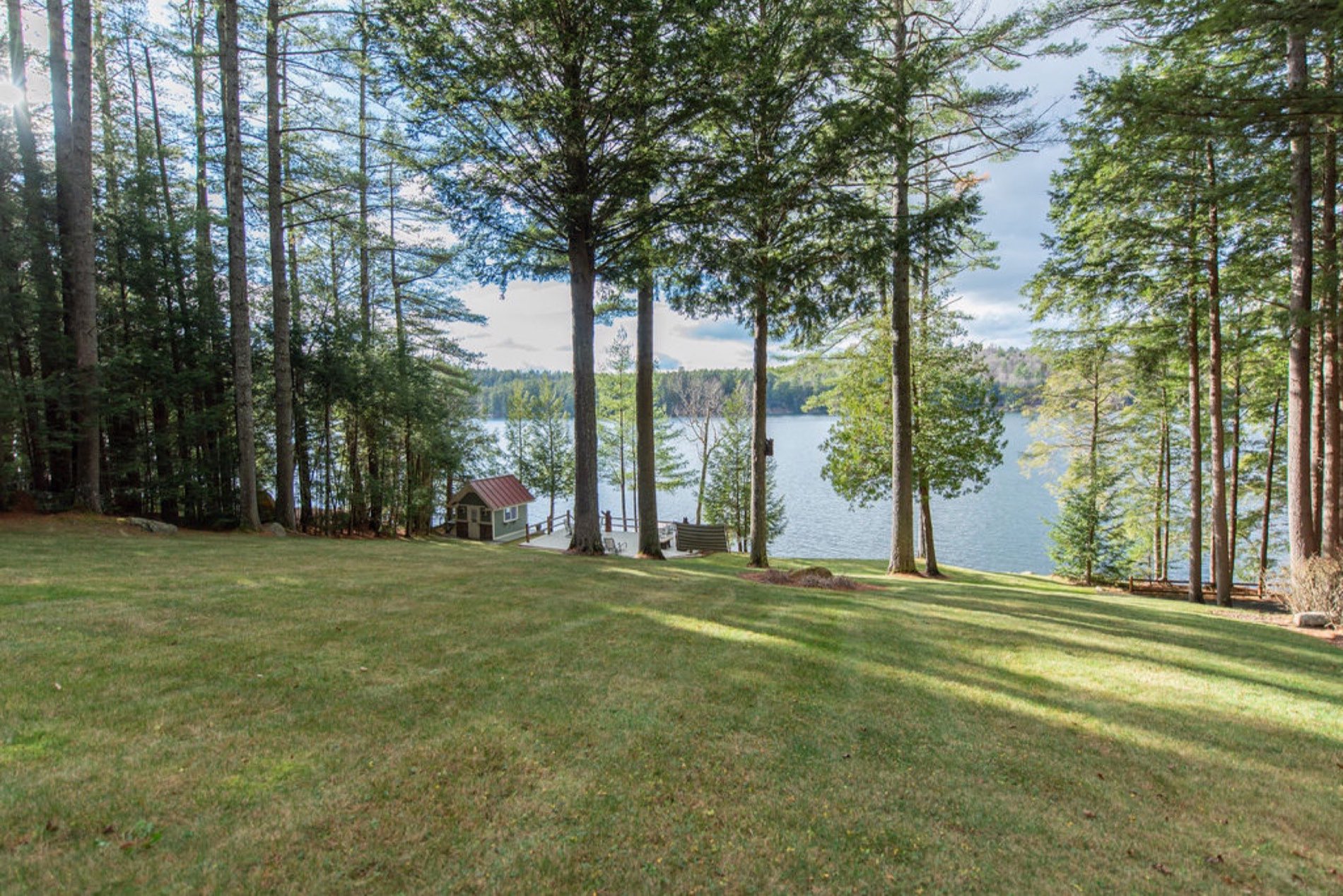 The lawn at Camp Sunnyside sloping through tall pines down to a dock and boathouse on Friends Lake in the Adirondacks.